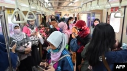 Para penumpang perempuan mengenakan masker di tengah wabah virus corona (Covid-19) di gerbong kereta commuter, di Jakarta, 7 April 2020. (Foto: AFP)