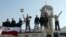 FILE - Soldiers loyal to the regime and civilians holding the Syrian national flag stand near boxes containing aid from the Syrian army in Qusair, June 5, 2013. 