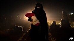 A woman who was evacuated out of the last territory held by Islamic State militants holds her baby after being screened by U.S.-backed Syrian Democratic Forces in the desert outside Baghuz, Syria, Feb. 25, 2019. 