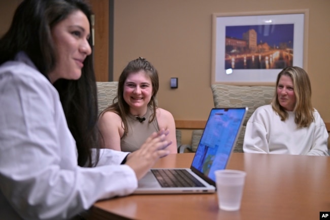 Alexis Bogan, center, and her mother Pamela Bogan, right, react to hearing a recreation of her lost voice from a prompt typed by Dr. Fatima Mirza, left, on Thursday, March 11, 2024, at Rhode Island Hospital in Providence, R.I. (AP Photo/Josh Reynolds)