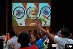 People wave India's national flag as India's Prime Minister Narendra Modi (C screen) congratulates the Indian Space Research Organisation (ISRO) for the successful lunar landing of Chandrayaan-3 spacecraft. (Photo by Punit PARANJPE / AFP)