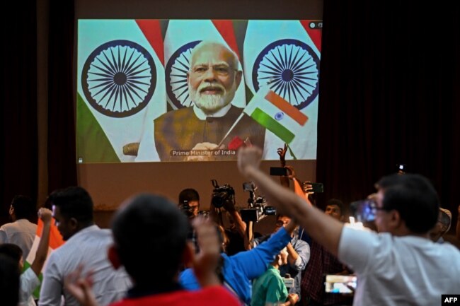 People wave India's national flag as India's Prime Minister Narendra Modi (C screen) congratulates the Indian Space Research Organisation (ISRO) for the successful lunar landing of Chandrayaan-3 spacecraft. (Photo by Punit PARANJPE / AFP)