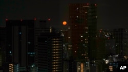 Tokyo's skyline is seen through the window of a hotel as the moon sets on July 23, 2021, in Tokyo. The opening ceremonies for the 2020 Summer Olympics are set for Friday.