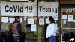 FILE - An Exam Corp Lab employee, right, wears a mask as she talks with a man lined up for COVID-19 testing, in Niles, Illinois, Oct. 21, 2020.