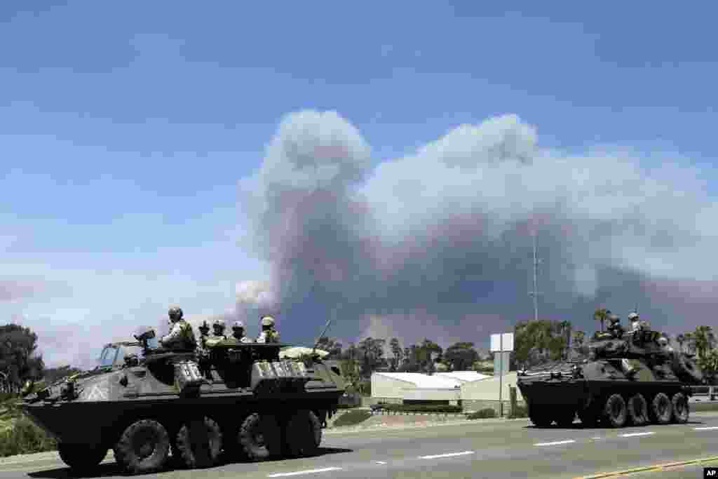 Marines move military vehicles near the entrance to Marine Corps Base Camp Pendleton in front of smoke plumes from the Las Pulgas wildfire burning on base, May 16, 2014.