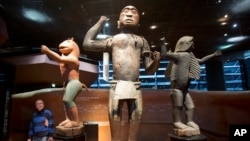 In this Friday, Nov. 23, 2018 file photo a visitor looks at wooden royal statues of the Dahomey kingdom, dated 19th century, at Quai Branly museum in Paris, France. 