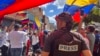 ARCHIVO - Un miembro de la prensa observa a manifestantes en una protesta política en Venezuela. 