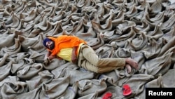 FILE - A farmer rests upon sacks filled with paddy at a wholesale grain market in Chandigarh, India.