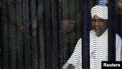 FILE - Sudan's former president Omar Hassan al-Bashir sits guarded inside a cage at the courthouse where he is facing corruption charges, in Khartoum, Aug. 19, 2019.