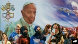 Women wait outside the Chaldean Cathedral of Saint Joseph in Baghdad, Iraq, March 6, 2021, where Pope Francis, depicted on a giant poster, is celebrating Mass. 