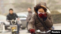 Una mujer usa máscara para desplazarse en su bicicleta en una calle de Beijing, donde la contaminación del aire es crítica con mucha frecuencia.