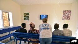 Seorang petugas UNHCR (tengah) berbicara dengan para pengungsi sembari menonton televisi di ruang tunggu kantor UNHCR di Niamey, Niger, 17 November 2017. Para pengungsi dievakuasi dari Libya. 