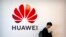In this Oct. 31, 2019, filer photo, a man uses his smartphone as he stands near a billboard for Chinese technology firm Huawei at the PT Expo in Beijing. (AP Photo/Mark Schiefelbein, File)