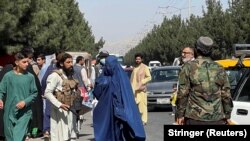 Taliban forces block the roads around the airport, while a woman with Burqa walks passes by in Kabul, on August 27, 2021. (Reuters)