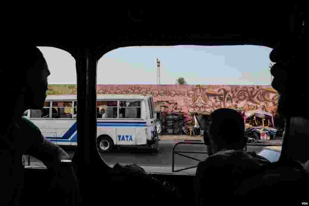 Passengers look out the window of a car rapide as an Indian-made Tata passes in Dakar, Senegal. (R. Shryock/VOA)