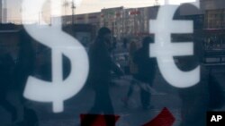 FILE - People walk along a street passing an exchange booth in downtown Moscow, Russia.