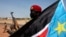 A soldier with the Sudan People's Liberation Army - the army of the Republic of South Sudan - is pictured behind a South Sudan flag as he sits on the back of a pick-up truck in Bentiu, Unity state, Jan. 12, 2014.