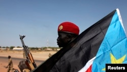 A South Sudanese soldier sits behind a South Sudan flag in Bentiu, Unity state, Jan. 12, 2014. South Sudan intercepted 11 U.N. trucks carrying weapons, headed to Bentiu. 