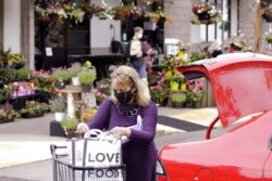 FILE - A woman wearing a mask loads groceries into her car in Portland, Ore., May 21, 2021. As the federal government and many states eased rules on mask-wearing and business occupancy this year, some blue states largely stuck with them.