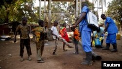 FILE - Children come forward to get their feet disinfected after a Red Cross worker explained that he was spraying bleach, and wasn't spraying the village with the Ebola virus, in Guinea's Forecariah district, Jan. 30, 2015.