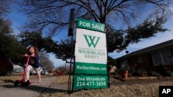 FILE - A girl pushes herself on a scooter by a home for sale in the Dallas suburb of Richardson, Texas, Feb. 28, 2019. 