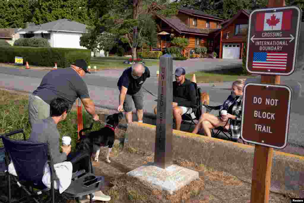 A man standing in Canada leans across the U.S.-Canada border to give a treat to a dog on the U.S. side after Canada opened the border to vaccinated Americans, in Blaine, Washington, Aug. 9, 2021.