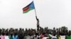 A man holds up South Sudan's new flag as South Sudanese children rehearse their dance routine, to be performed at half time during South Sudan's national soccer team's match with Kenya as part of the independence day celebrations. Photo by Paul Banks, 