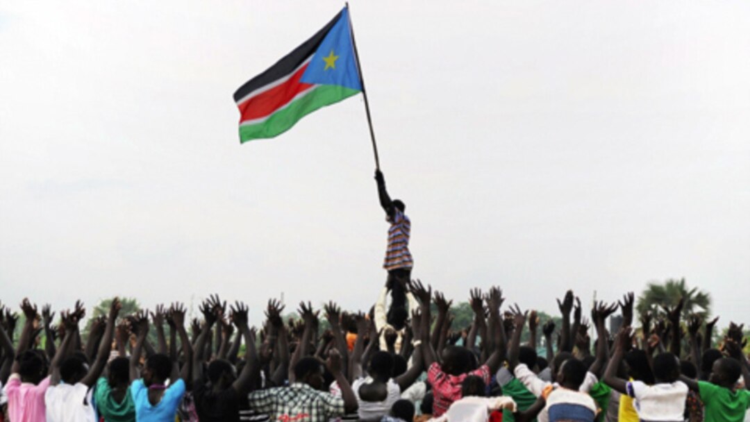 A man holds up South Sudan's new flag as South Sudanese children rehearse their dance routine, to be performed at half time during South Sudan's national soccer team's match with Kenya as part of the independence day celebrations. Photo by Paul Banks, 
