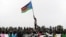 A man holds up South Sudan's new flag as South Sudanese children rehearse their dance routine, to be performed at half time during South Sudan's national soccer team's match with Kenya as part of the independence day celebrations.    Photo by Paul Banks, 
