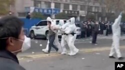 In this photo provided Nov 23, 2022, security personnel in protective clothing were seen taking away a person during protest at the factory compound operated by Foxconn Technology Group in Zhengzhou, China.