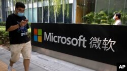 FILE - A man looks at his smartphone as he walks by the Microsoft office in Beijing, China, Aug. 7, 2020. The Biden administration on July 19, 2021 blamed China for a hack of Microsoft Exchange email server software earlier this year.