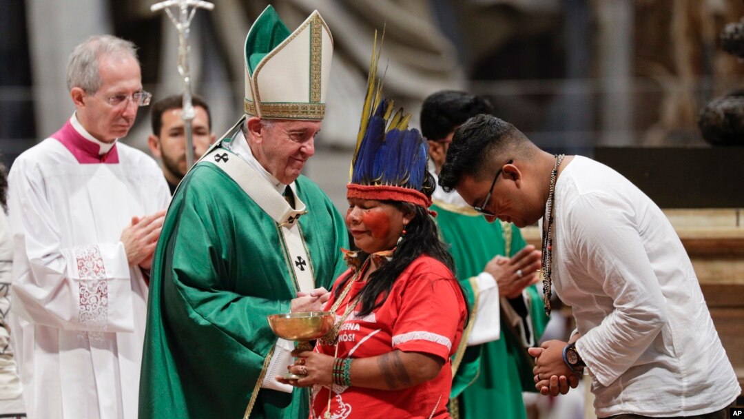 Masyarakat adat, beberapa dengan wajah dicat dan mengenakan hiasan kepala, berdiri di sebelah Paus Fransiskus saat misa untuk Amazon di Basilika Santo Petrus, di Vatikan, 6 Oktober 2019. (Foto: AP)