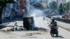 Un motociclista pasa al lado de un contenedor de basura quemado durante las protestas populares de este lunes contra el resultado oficial de la elección presidencial en Venezuela, en Caracas, la mañana del martes 30 de julio de 2024.