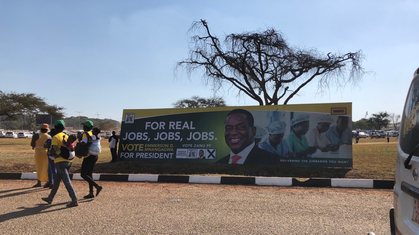 Members of ZANU-PF walk past their party’s poster at a rally in Harare with promises for jobs if President Mnangagwa wins prevails in the election, July 28, 2018. 