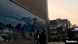 FILE - People walk past an advertisement near the flagship store of Canadian luxury parka maker Canada Goose in Beijing, China, Dec. 31, 2018. 