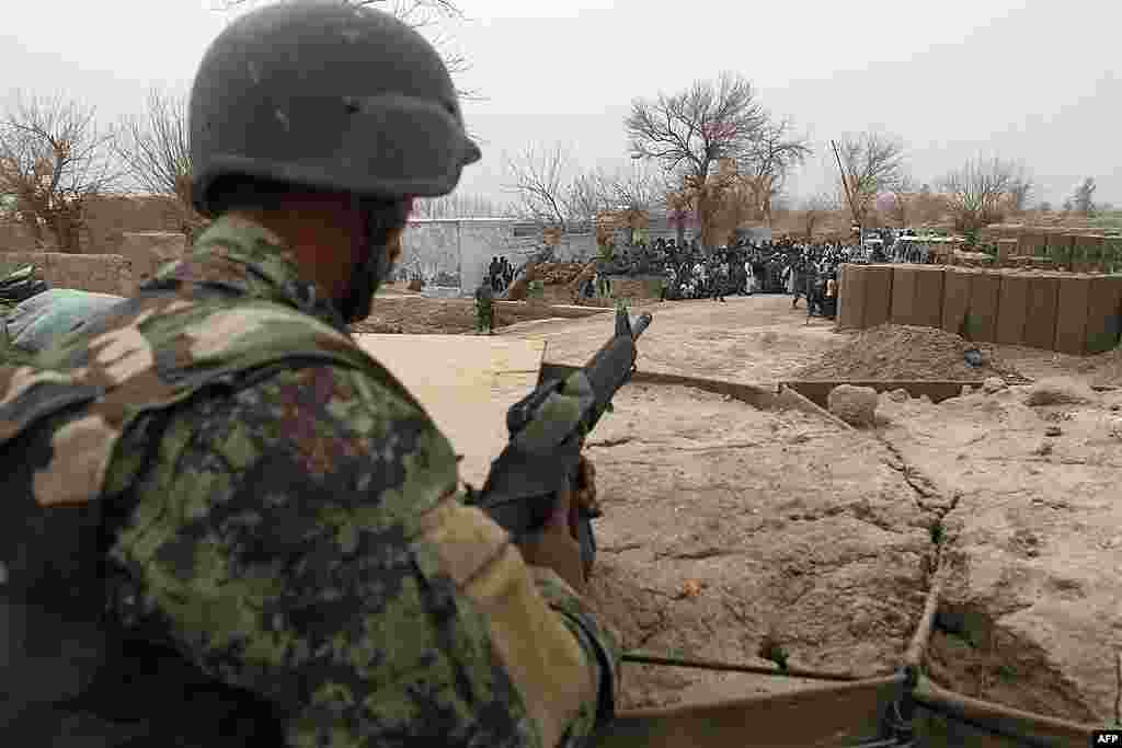 An Afghan soldier is seen in a guard tower at a military base as civilians gather outside in Panjwai. (AP)