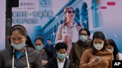 FILE - People wearing protective face masks walk on a street in the Central, the business district of Hong Kong, Feb. 11, 2020. 