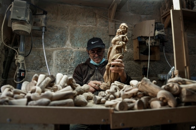 A Palestinian craftsman carves a figurine of the Virgin Mary and baby Jesus, in the West Bank town of Bethlehem, at the beginning of the Christmas season, Saturday, Dec. 3, 2022. (AP Photo/ Mahmoud Illean)