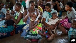 FILE - Women wait to have their children vaccinated against malaria wait at an inoculation site in the Malawi village of Tomali, Dec. 11, 2019.