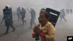 A protester escapes from riot police officers who fire tear gas grenades during a protest in Phnom Penh, Jan. 27, 2014.