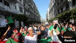 FILE - Demonstrators carry national flags as they protests calling for a complete overhaul of the ruling elite, an end to corruption and the army's withdrawal from politics, in Algiers, Feb. 14, 2020.