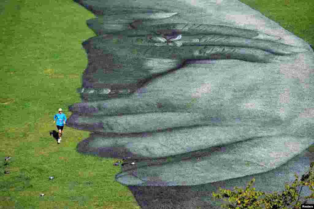 A man jogs next to the artwork of French street artist Saype, called &quot;Beyond Walls,&quot; a spray paint series of interlocked hands, painted across the grass in front of the Palatine Gate, in Turin, Italy, Sept. 30, 2020.