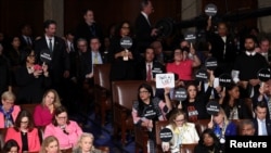 People hold protest signs during U.S. President Donald Trump's speech to a joint session of Congress, in the House Chamber of the U.S. Capitol in Washington, March 4, 2025.