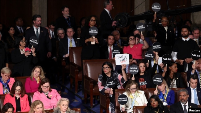 People hold protest signs during U.S. President Donald Trump's speech to a joint session of Congress, in the House Chamber of the U.S. Capitol in Washington, March 4, 2025.