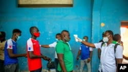 Health ministry workers check the temperature of mask-wearing fans as a precaution against the spread of the new coronavirus, before entering the stadium prior to the start of the CONCACAF World Cup qualifying soccer match between Haiti and Belize.