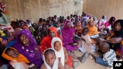 FILE - Women and children wait to participate in a vaccination campaign against meningitis at the community center in Al Neem camp for Internally Displaced People in El Daein, East Darfur, Sudan, October 8, 2012.