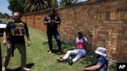 FILE - Two men, on the ground, suspected of driving a stolen vehicle, are apprehended by private security personal in a suburb east of Johannesburg, South Africa, December 1, 2023