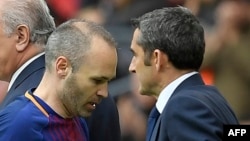 Le milieu de terrain espagnol de Barcelone Andres Iniesta, à gauche, passe devant le sélectionneur espagnol de Barcelone Ernesto Valverde lors du match de foot entre le FC Barcelona et le Valencia CF au Camp Nou de Barcelone le 14 avril 2018. 