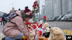 Một em nhỏ đặt một món đồ chơi ở hàng rào cạnh nhà hát Crocus City Hall, ở rìa phía tây của Moscow, Nga, hôm Thứ Bảy, ngày 23 tháng 3 năm 2024, để tưởng nhớ các nạn nhân vụ xả súng hôm thứ Sáu mà nhóm Nhà nước Hồi giáo đã nhận trách nhiệm.
