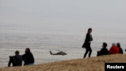 People look on as an Israeli rescue helicopter operates near the site where a group of Israeli youths was swept away by a flash flood, near the Zafit river bed, south of the Dead Sea, Israel, April 26, 2018. 